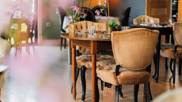 A dining area with wooden tables, cushioned chairs, and a vase with flowers.