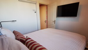 A hotel room with a bed, a TV mounted on the wall, and a door leading to another room. - Hôtel Mercator (Vendome)