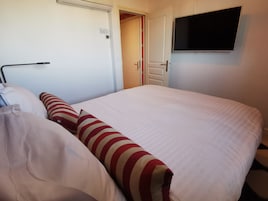 Una habitación de hotel con una cama, un televisor fijado a la pared y una puerta que da a otra habitación.