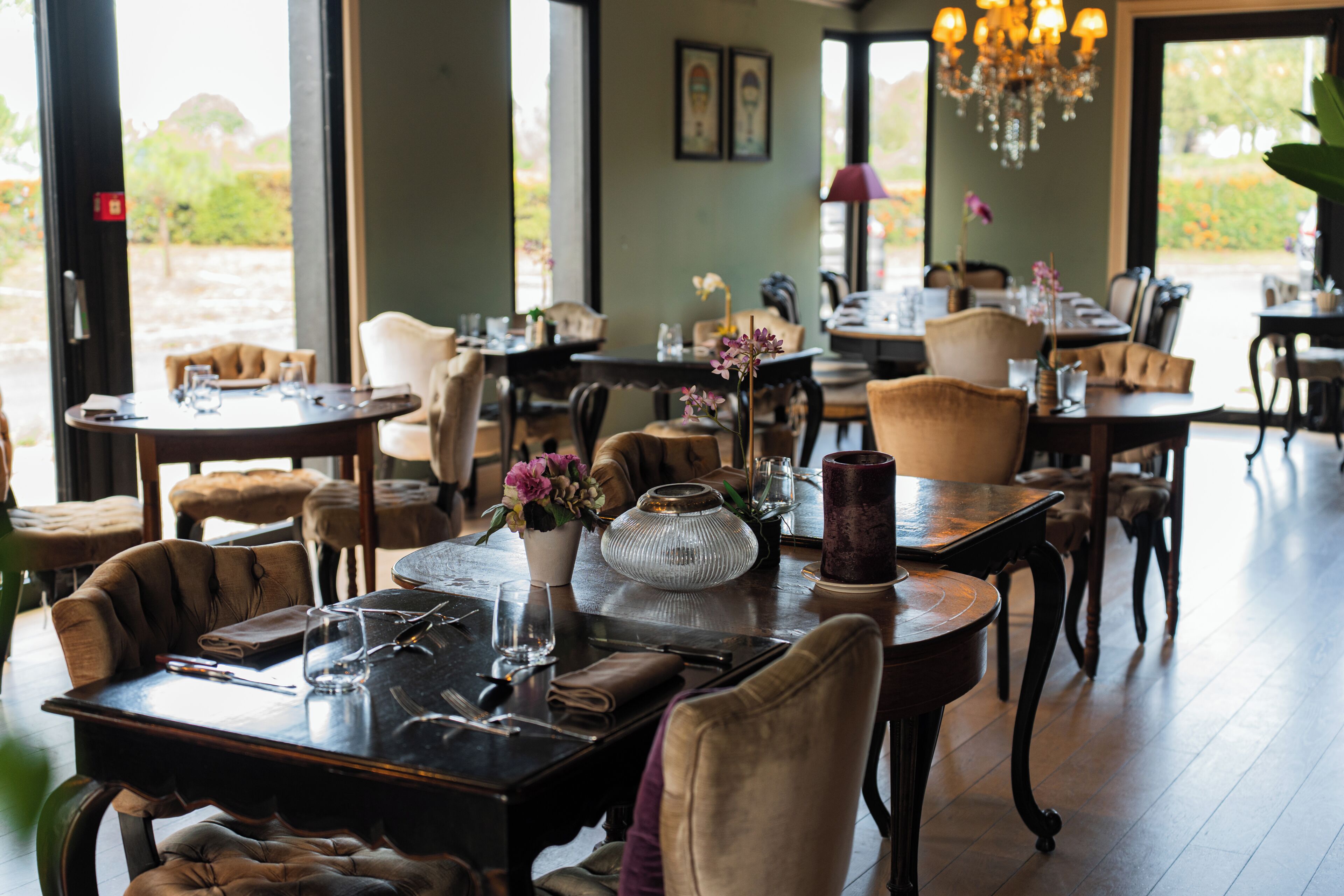 Un restaurant doté de nombreuses tables et chaises, d’un lustre et offrant une vue sur l’extérieur grâce à de grandes fenêtres.