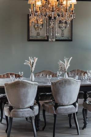 A dining area with a chandelier, a long table, and upholstered chairs.