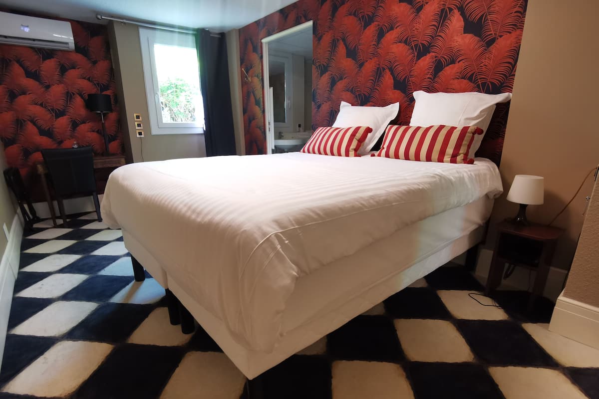 Una habitación de hotel con una cama grande, suelo a cuadros, un escritorio y una ventana con cortinas.
