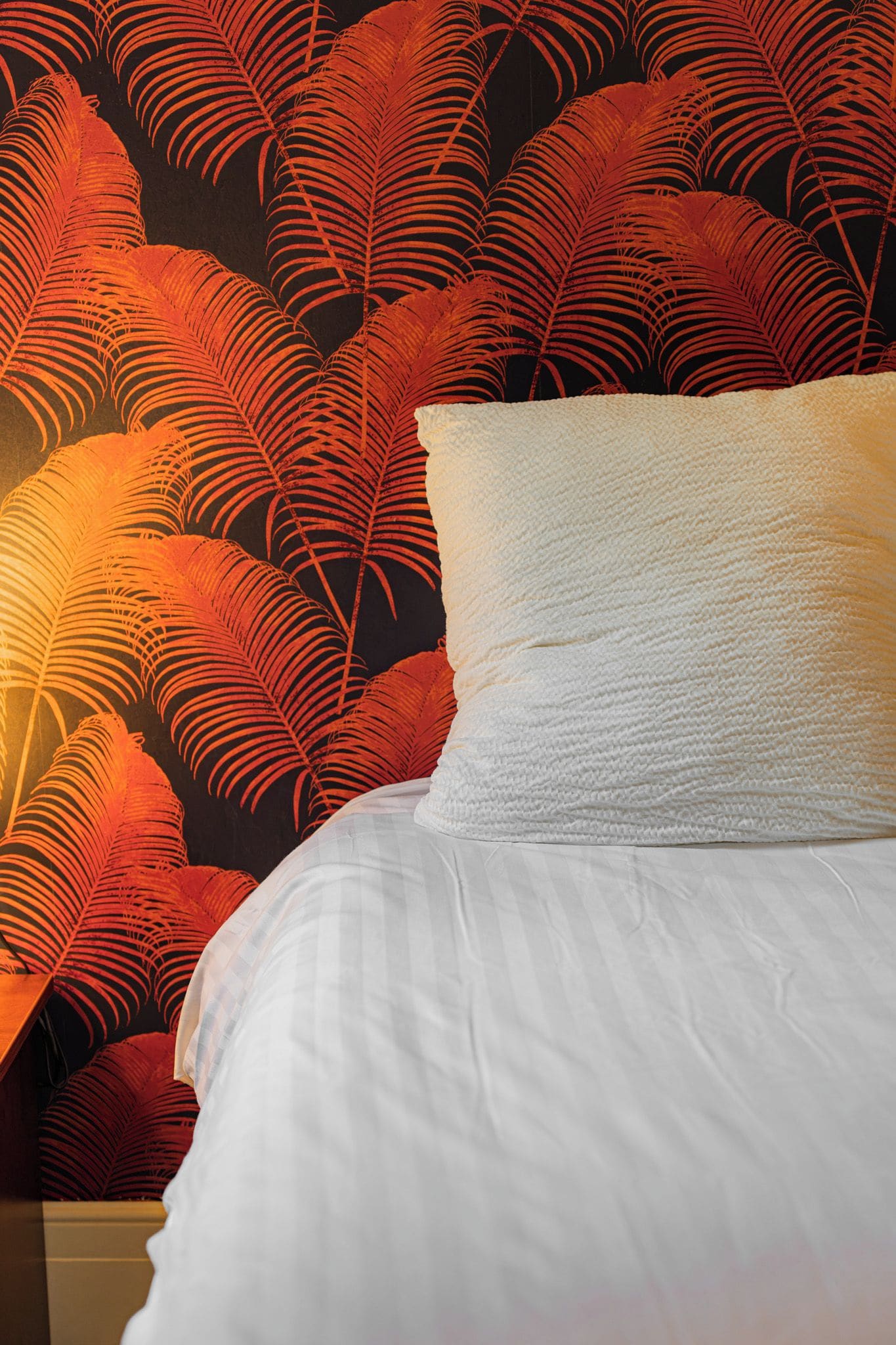 A bed with white bedding and a pillow, set against a wall with a red and black leaf pattern.