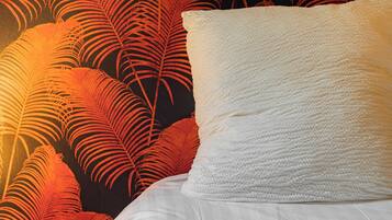A bed with white bedding and a pillow, set against a wall with a red and black leaf pattern.