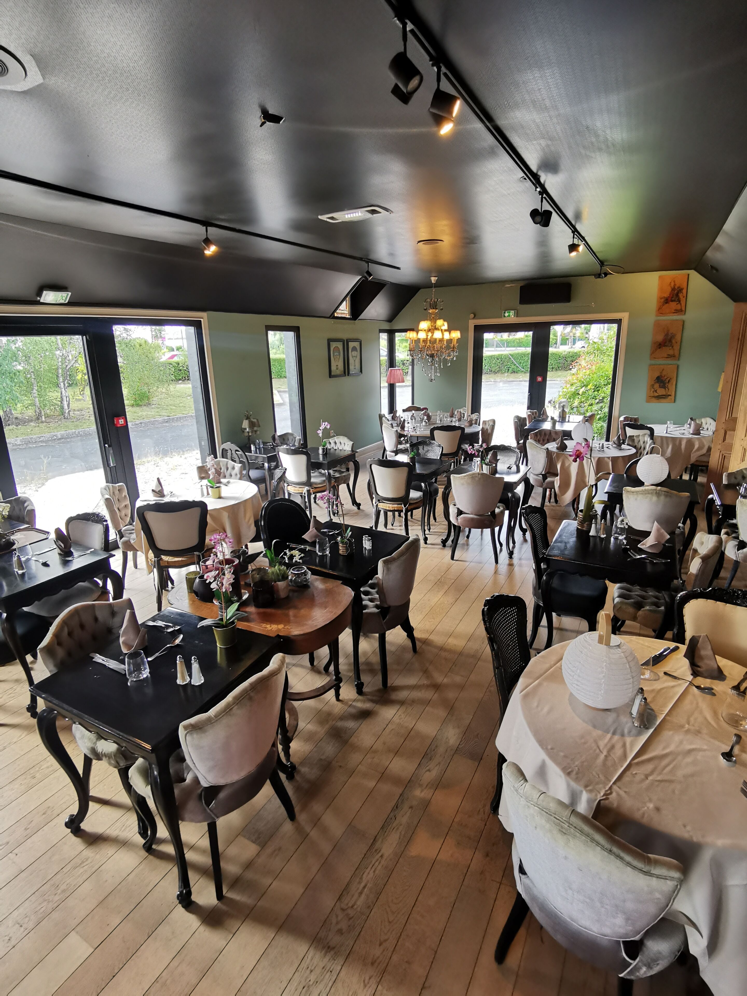Un restaurant doté de nombreuses tables et chaises, de grandes fenêtres et d’un lustre.
