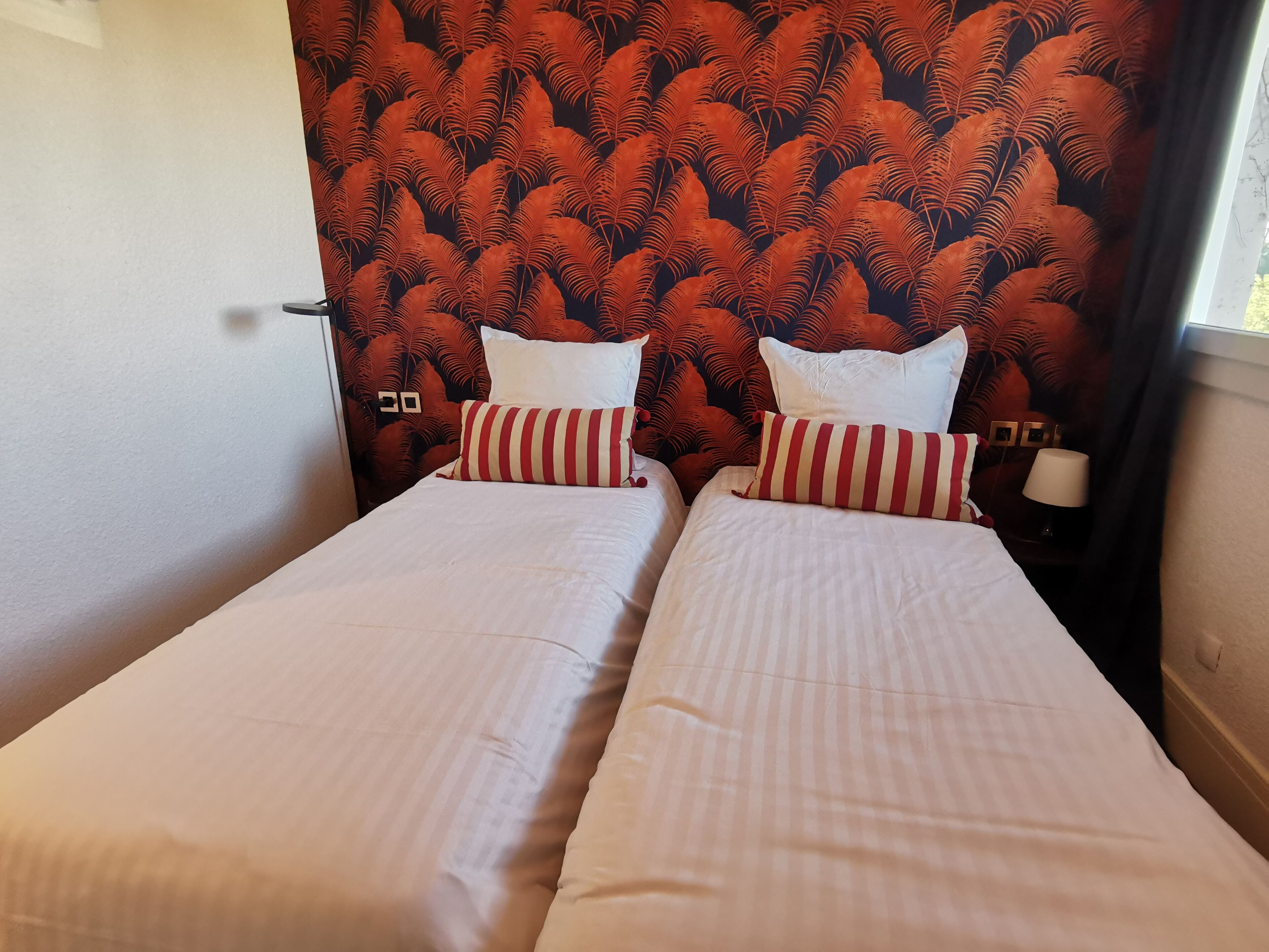 A room with two beds, a patterned headboard, and a nightstand with a lamp.