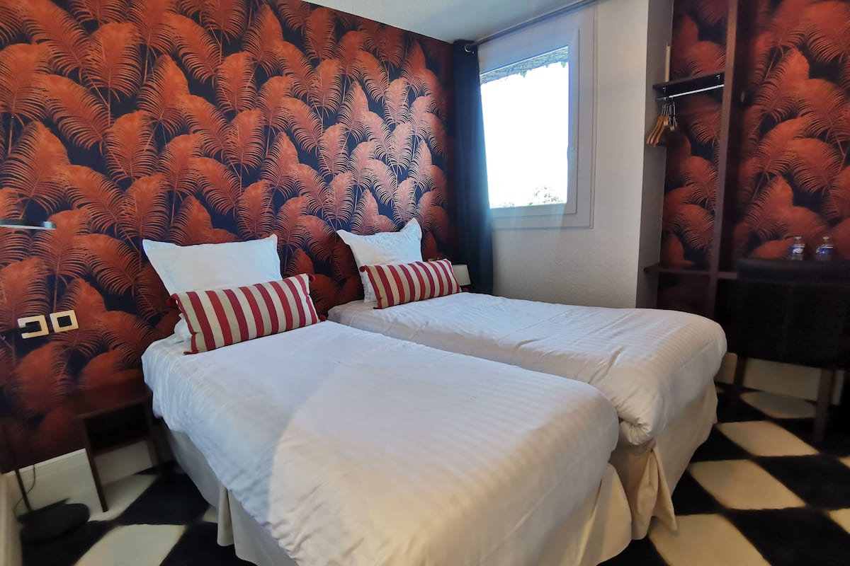 Habitación de hotel con dos camas, suelo a cuadros y pared decorada con un diseño de hojas.