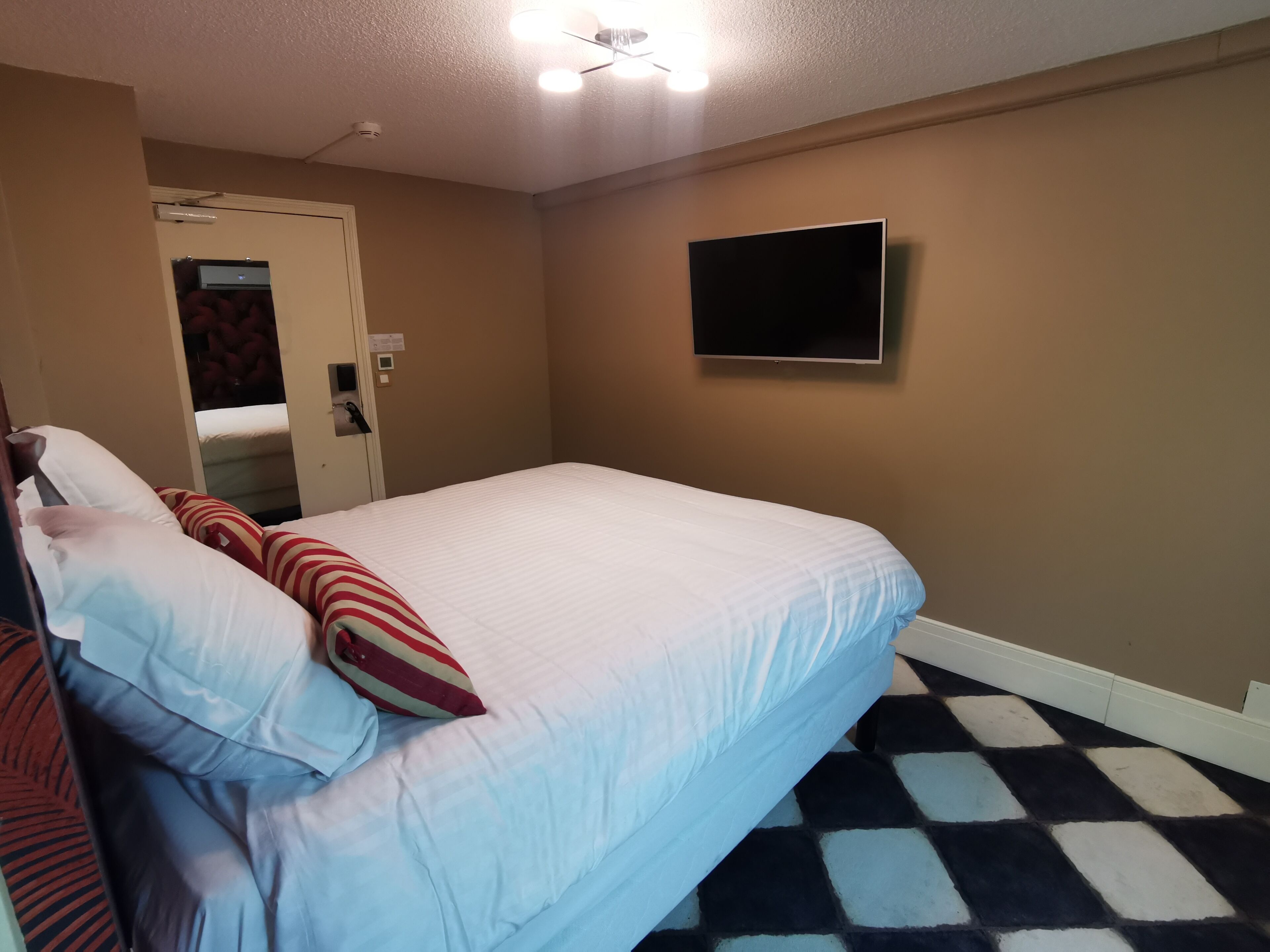 Habitación de hotel con cama, televisión de pantalla plana en la pared y suelo estampado.