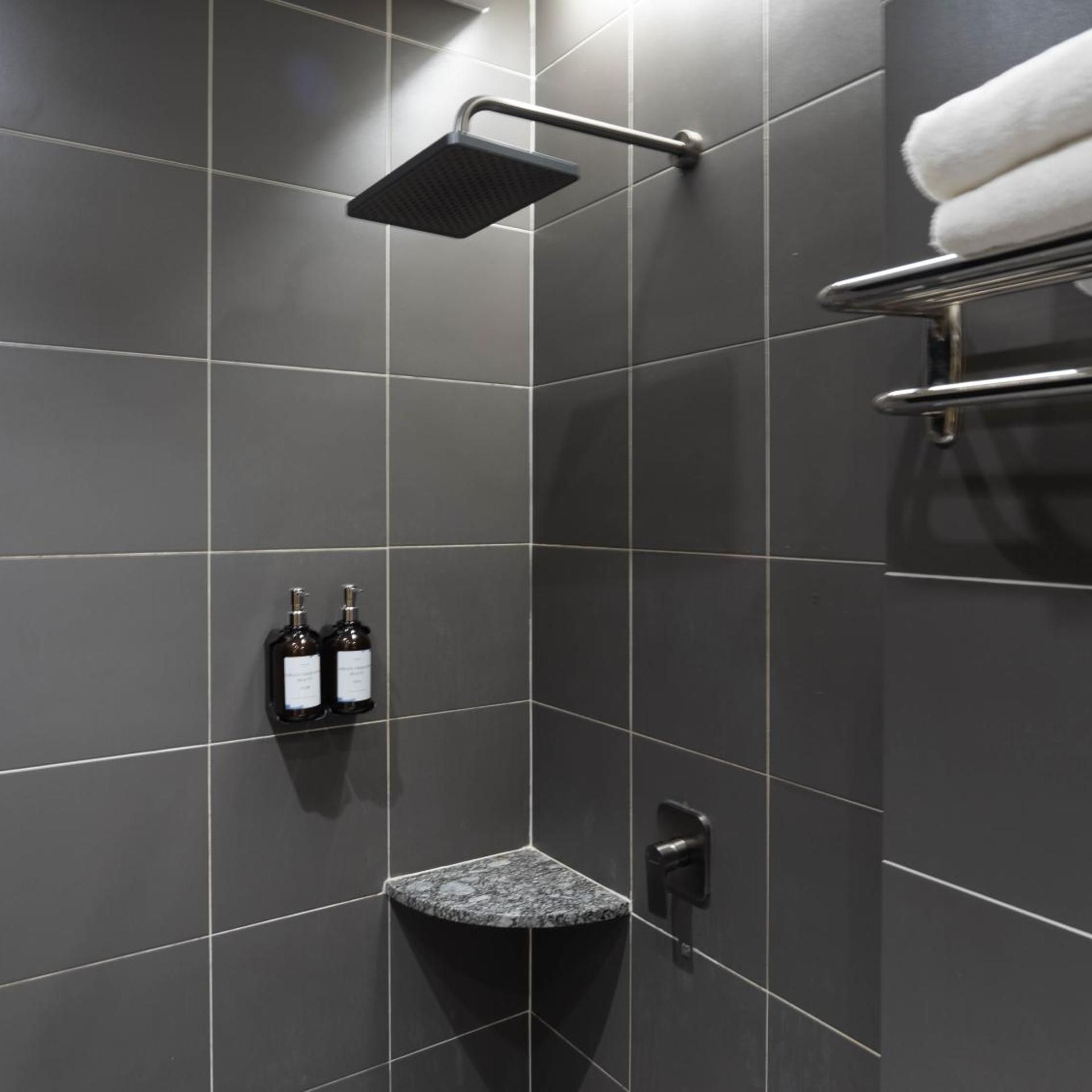 A modern bathroom with dark tiles, a shower, a towel rack, and two bottles of shampoo.