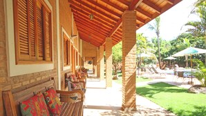 A covered outdoor seating area with wooden benches and a stone wall. - Pousada Faruk (Olímpia)