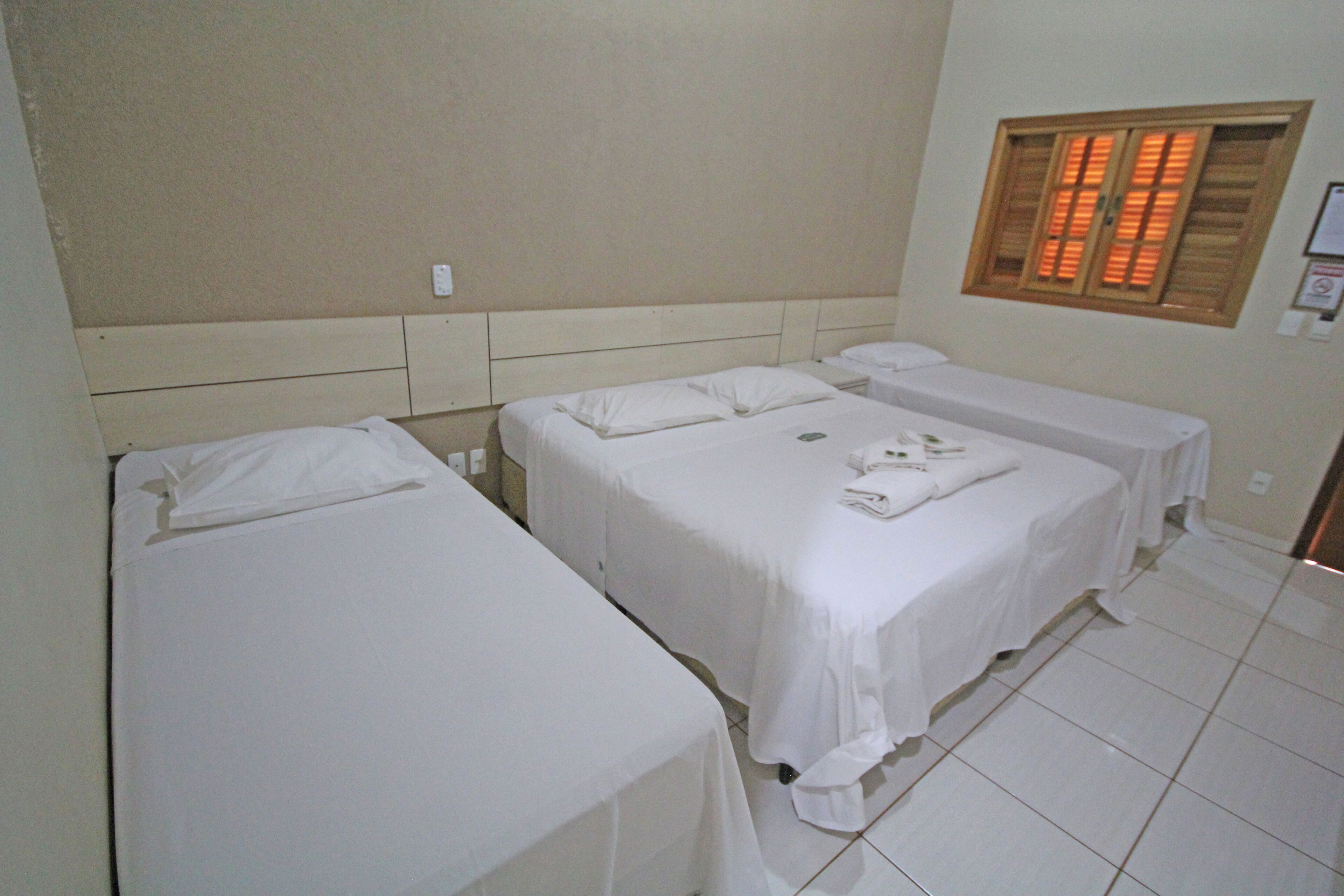 A hotel room with three single beds, a small table, and a window with shutters.