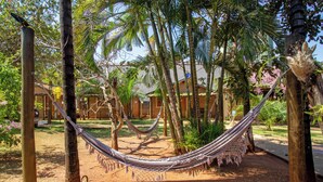 A hammock between trees in a garden with a building in the background. - Pousada Faruk (Olímpia)