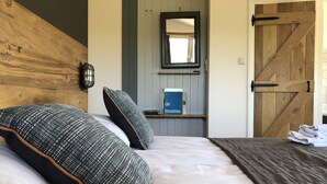 A bedroom with a wooden headboard, a large bed with patterned pillows, a bedside table with a book, and a wooden door. - Hotel de Plank (Noorbeek)