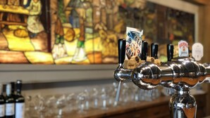 A bar with a tap and glasses, a stained glass window, and bottles of wine. - Hotel de Plank (Noorbeek)
