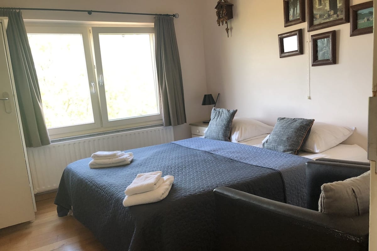 Un dormitorio con una cama grande, dos mesitas de noche, una ventana con cortinas y cuadros en la pared.