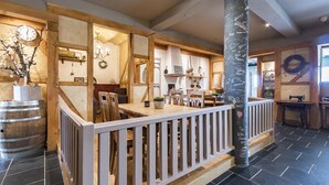 A spacious dining area with a wooden railing, a large clock, and a black column with writings. - Hotel de Plank (Noorbeek)