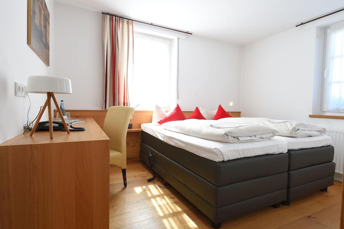 Een hotelkamer met een bed, een bureau met lamp, een stoel en een raam met gordijnen.
