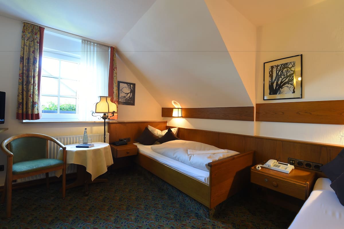 Een hotelkamer met een bed, een stoel, een tafel, een lamp en een raam met gordijnen.