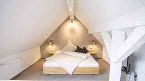 Une chambre à coucher moderne et minimaliste, dotée d’un plafond en pente, d’un cadre de lit en bois et de lampes de chevet.