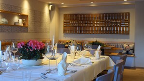 Un espace repas avec des tables dressées pour le repas, un mur décoratif et une étagère avec divers objets.
