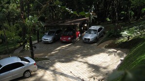 A parking area with multiple cars, a covered shelter, and a paved walkway surrounded by greenery. - Chalé da Floresta (Camanducaia)