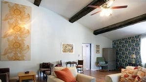 A living room with a high ceiling, exposed beams, and a ceiling fan. There are two sofas, a coffee table, and a painting on the wall. - La Maison de Textile (Montolieu)