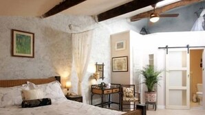 A bedroom with a large bed, a ceiling fan, and a view of the bathroom. - La Maison de Textile (Montolieu)