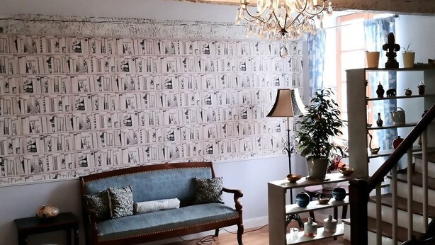 A living room with a patterned wallpaper, a blue sofa, a chandelier, and a staircase with shelves. - La Maison de Textile (Montolieu)