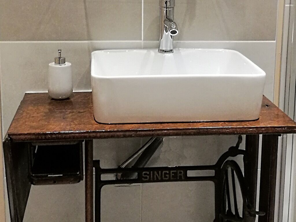 Un lavabo blanco sobre una mesa de madera con estructura metálica que dice 'SINGER'.