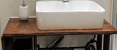 Un lavabo blanco sobre una mesa de madera con estructura metálica que dice 'SINGER'.
