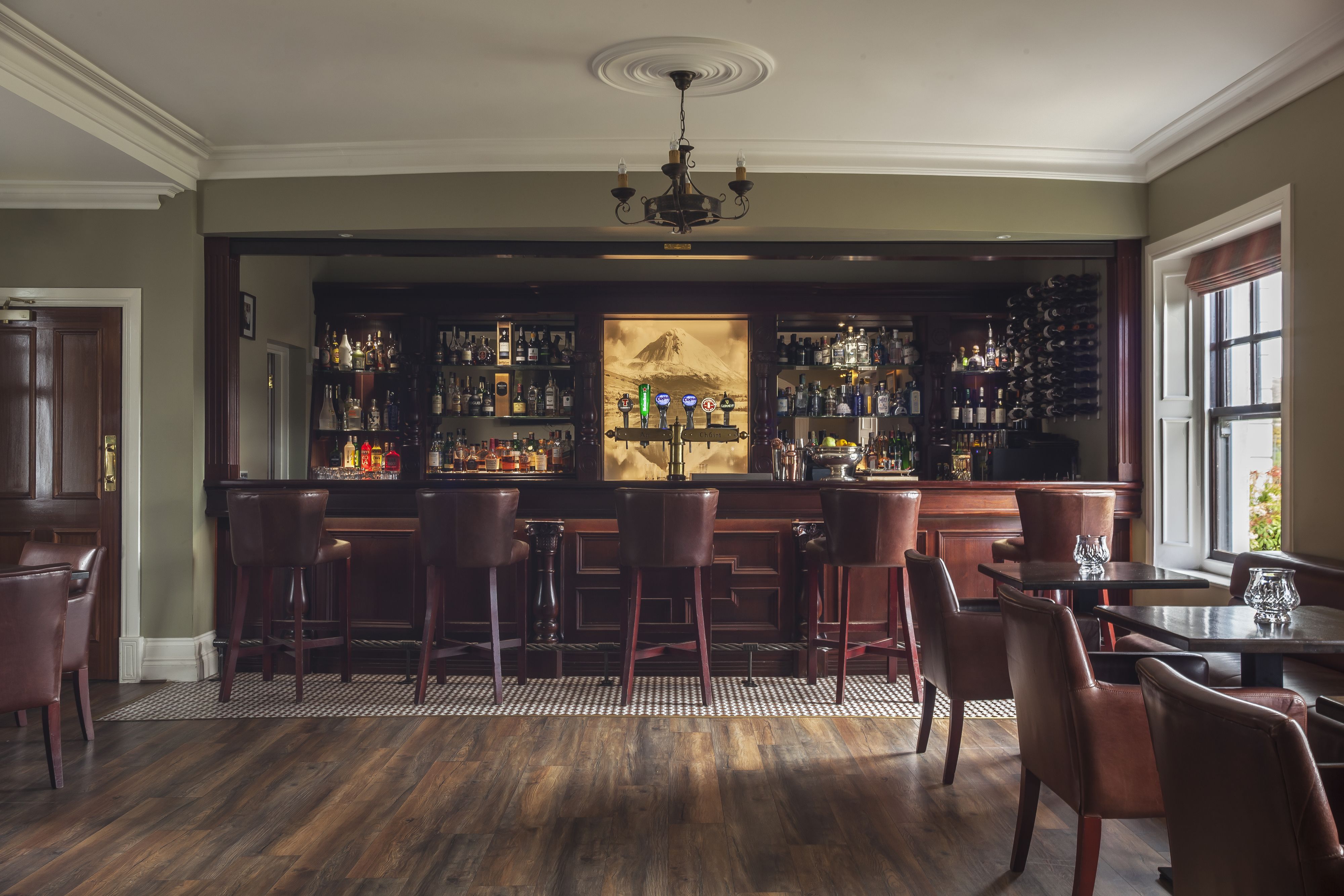 A bar area with wooden bar stools, a chandelier, and a wine rack.