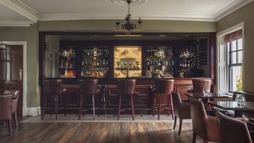 A bar area with wooden bar stools, a chandelier, and a wine rack.