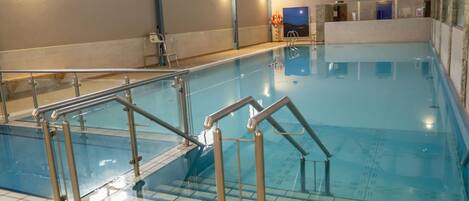 An indoor swimming pool with clear water, metal railings, and tiled flooring.