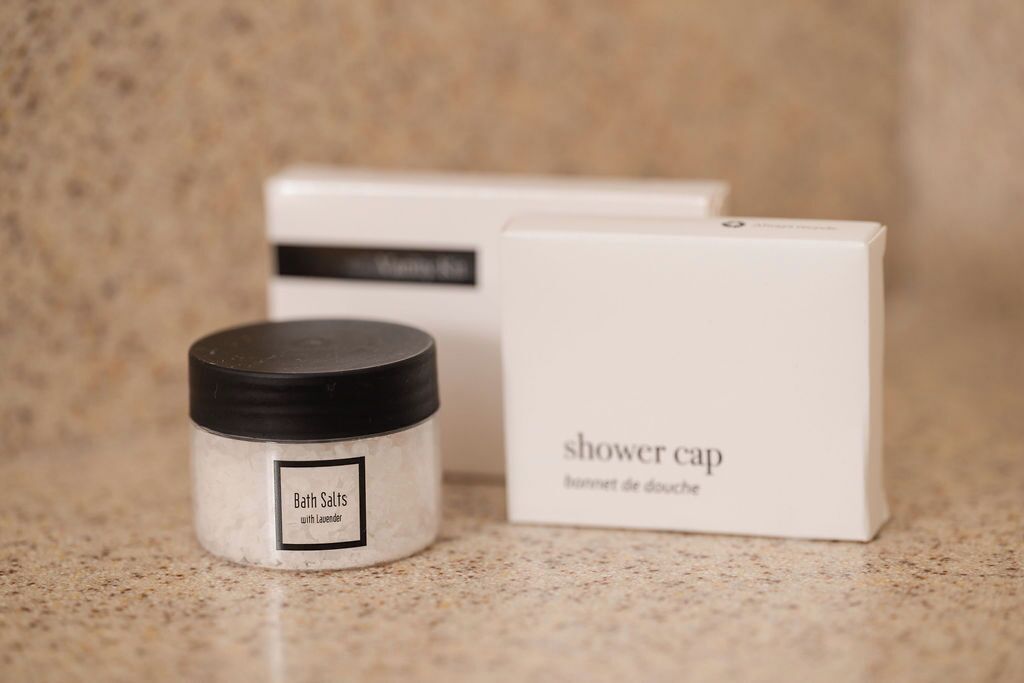 A container of bath salts with a label and a box labeled 'shower cap' in the background.