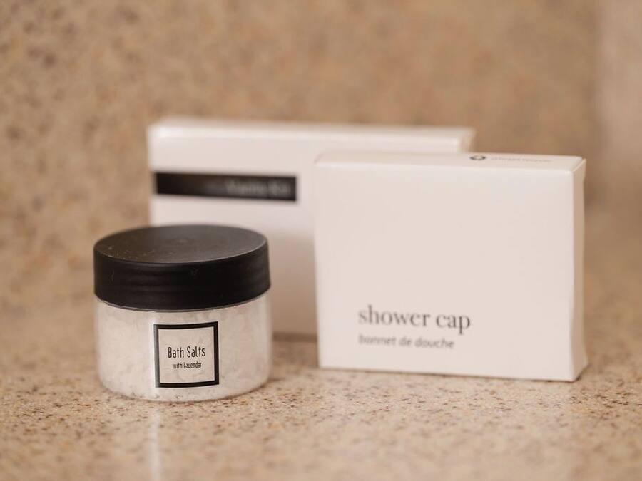 A container of bath salts with a label and a box labeled 'shower cap' in the background.