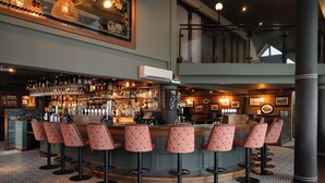 A bar area with a high bar counter, multiple stools, and a variety of bottles and glasses. - An Chúirt Hotel (Gweedore)