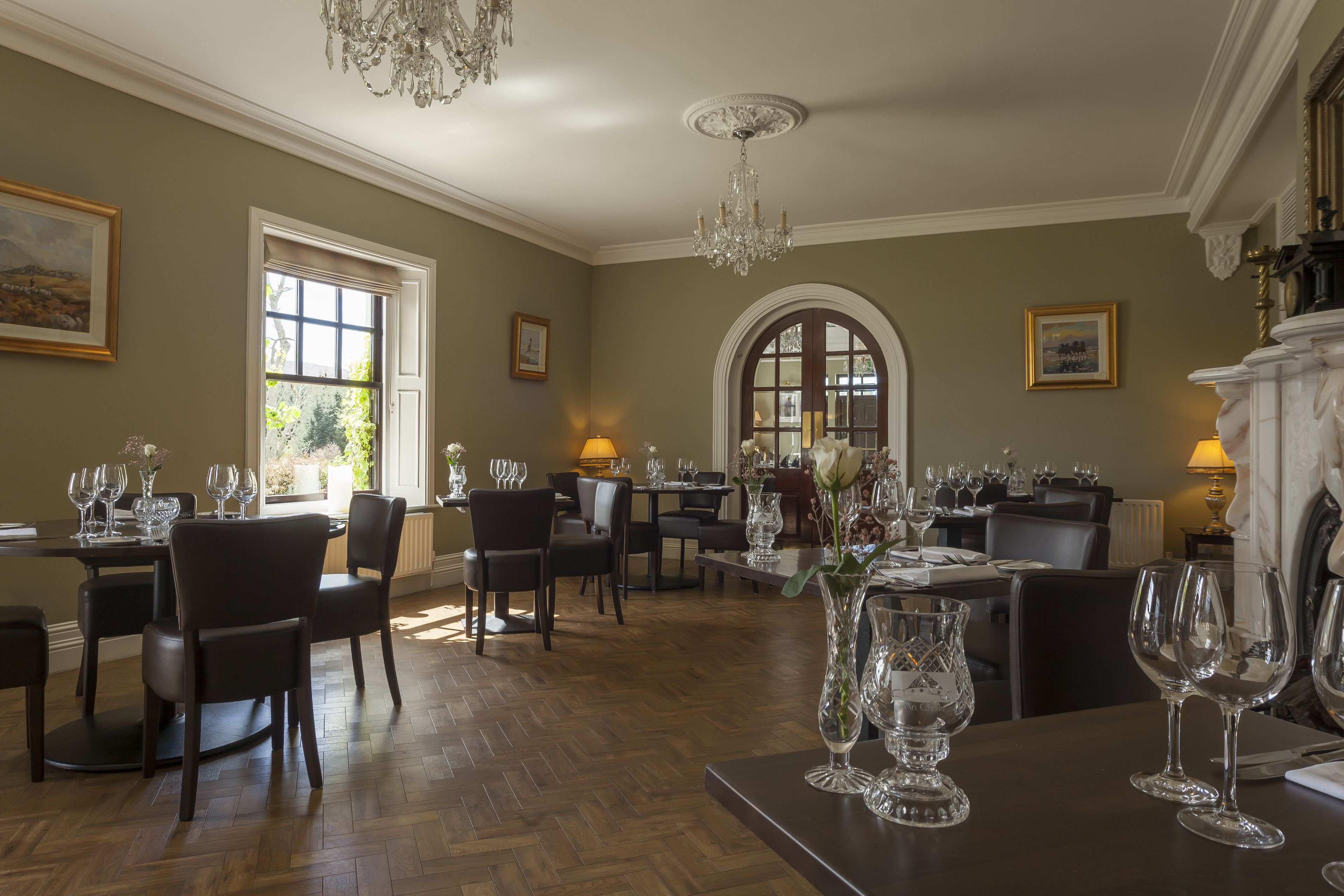 A dining area with multiple tables set for guests, featuring elegant chairs and a chandelier.