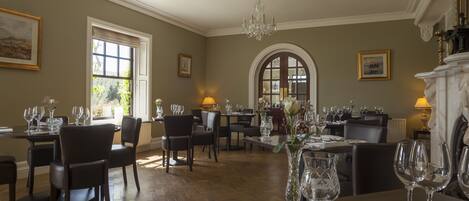 A dining area with multiple tables set for guests, featuring elegant chairs and a chandelier.