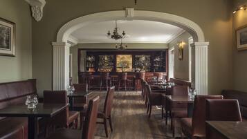 A restaurant with a central bar area, wooden tables and chairs, and a chandelier.