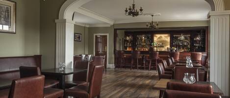 A bar area with wooden flooring, leather seating, and a bar stocked with bottles.