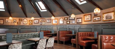 En restaurant med højt til loftet, ovenlysvinduer og forskellige siddepladser, herunder både båse og borde.