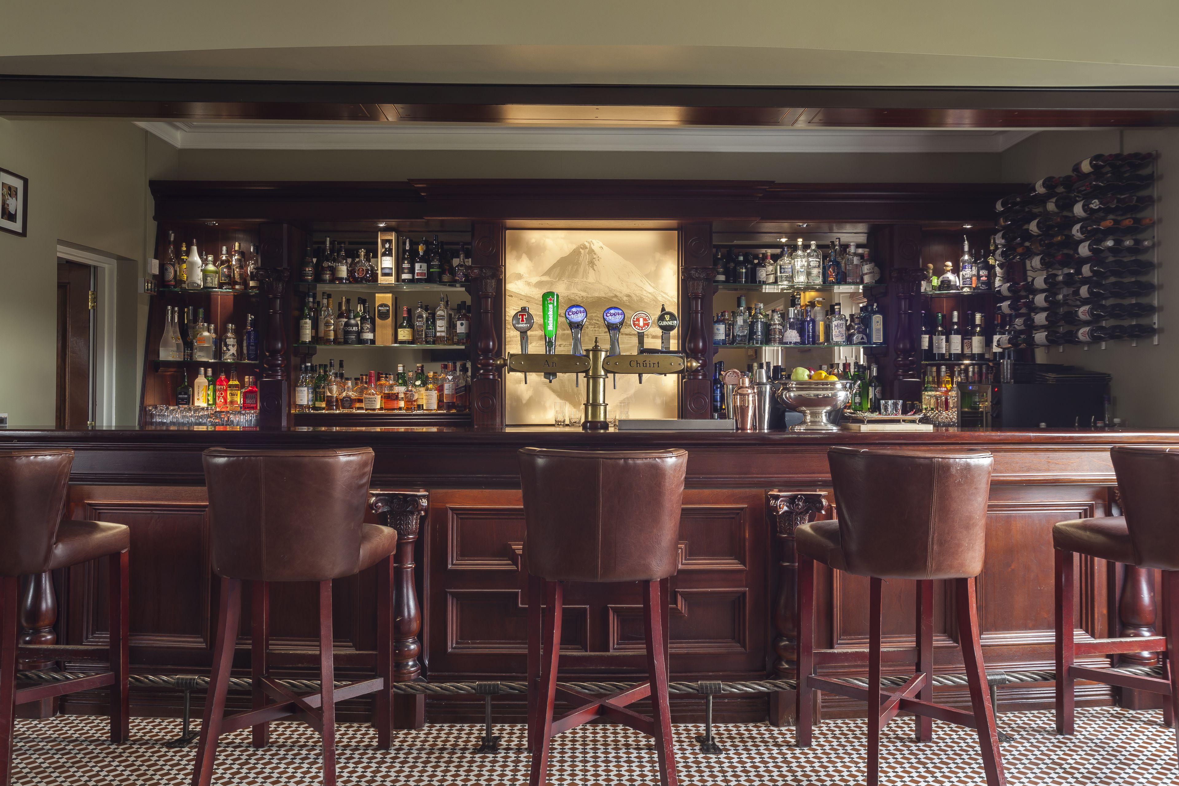 A bar area with wooden bar stools, a variety of liquor bottles, and a wall-mounted wine rack.