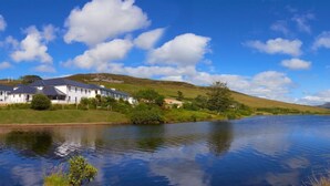 A riverside view with a white building, a hill, and a mountain in the background. - An Chúirt Hotel (Gweedore)