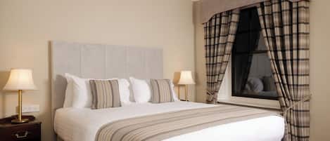 A neatly made bed with a striped bedspread, two bedside lamps, and a window with plaid curtains.