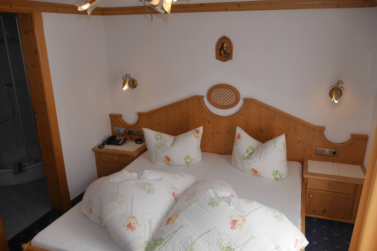 Una cama con estructura de madera, ropa de cama floral, mesitas de noche con lámparas y un aplique de pared.