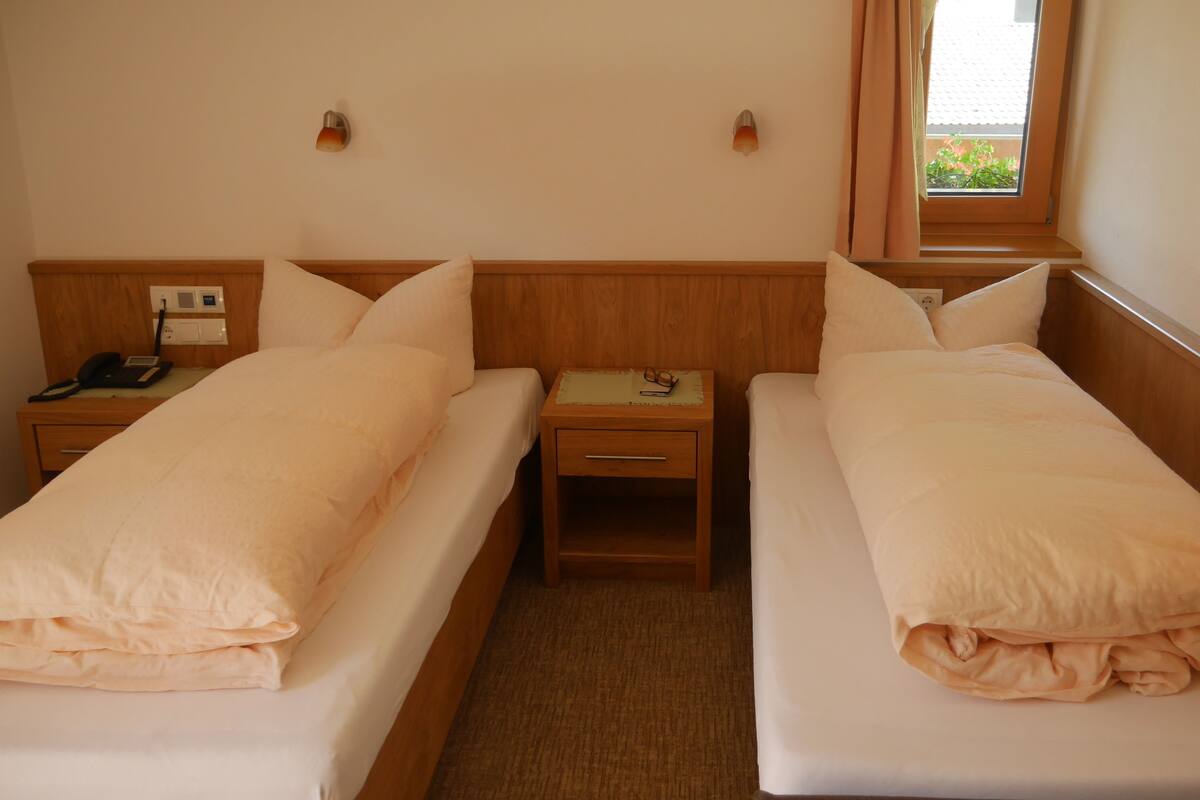 Habitación de hotel con dos camas individuales, una mesita de noche con lámpara, teléfono y ventana con cortinas.