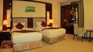 Een hotelkamer met twee bedden, een bureau, een stoel en een schilderij aan de muur.
