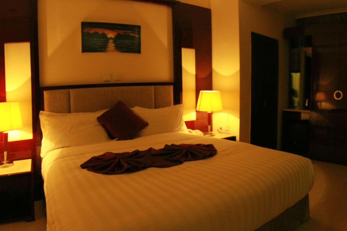 A hotel room with a large bed, two bedside lamps, a nightstand, and a painting on the wall.