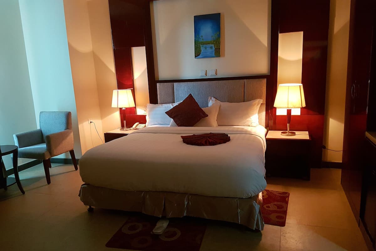 A hotel room with a large bed, two bedside lamps, a painting on the wall, and a chair.