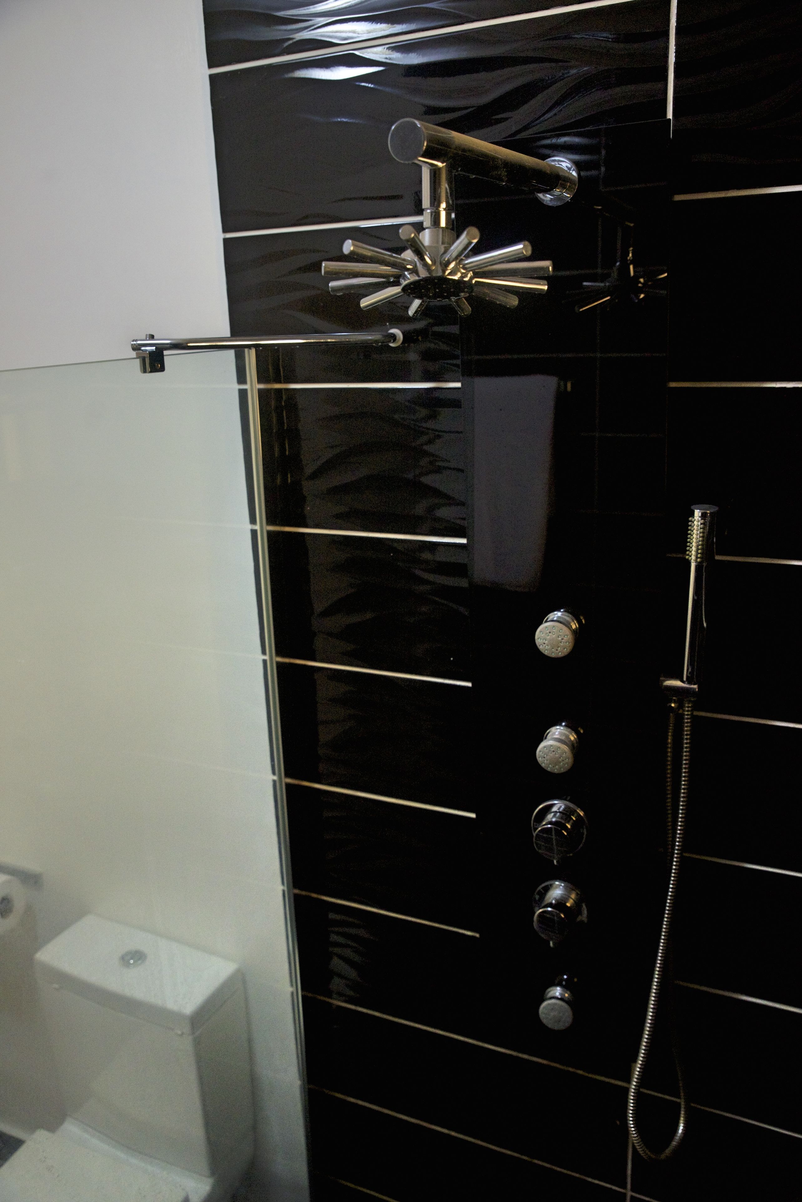 Un bagno con parete piastrellata di nero, soffione cromato e doccetta manuale.